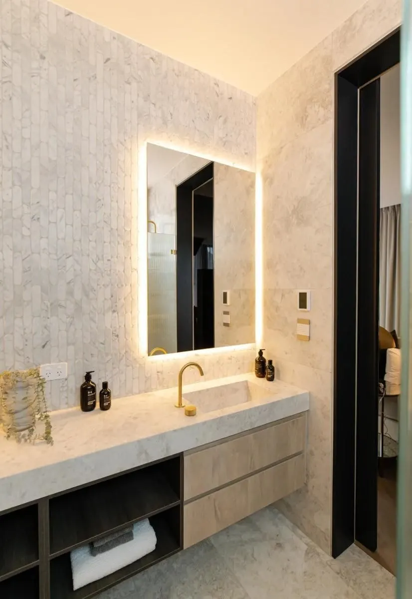 Ensuite with a floating timber vanity with open shelf, backlit mirror and marble mosaic feature wall