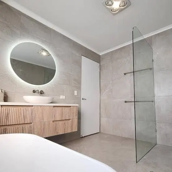 Bathroom renovation with a fluted timber floating vanity, backlit round mirror, frameless shower and freestanding bath