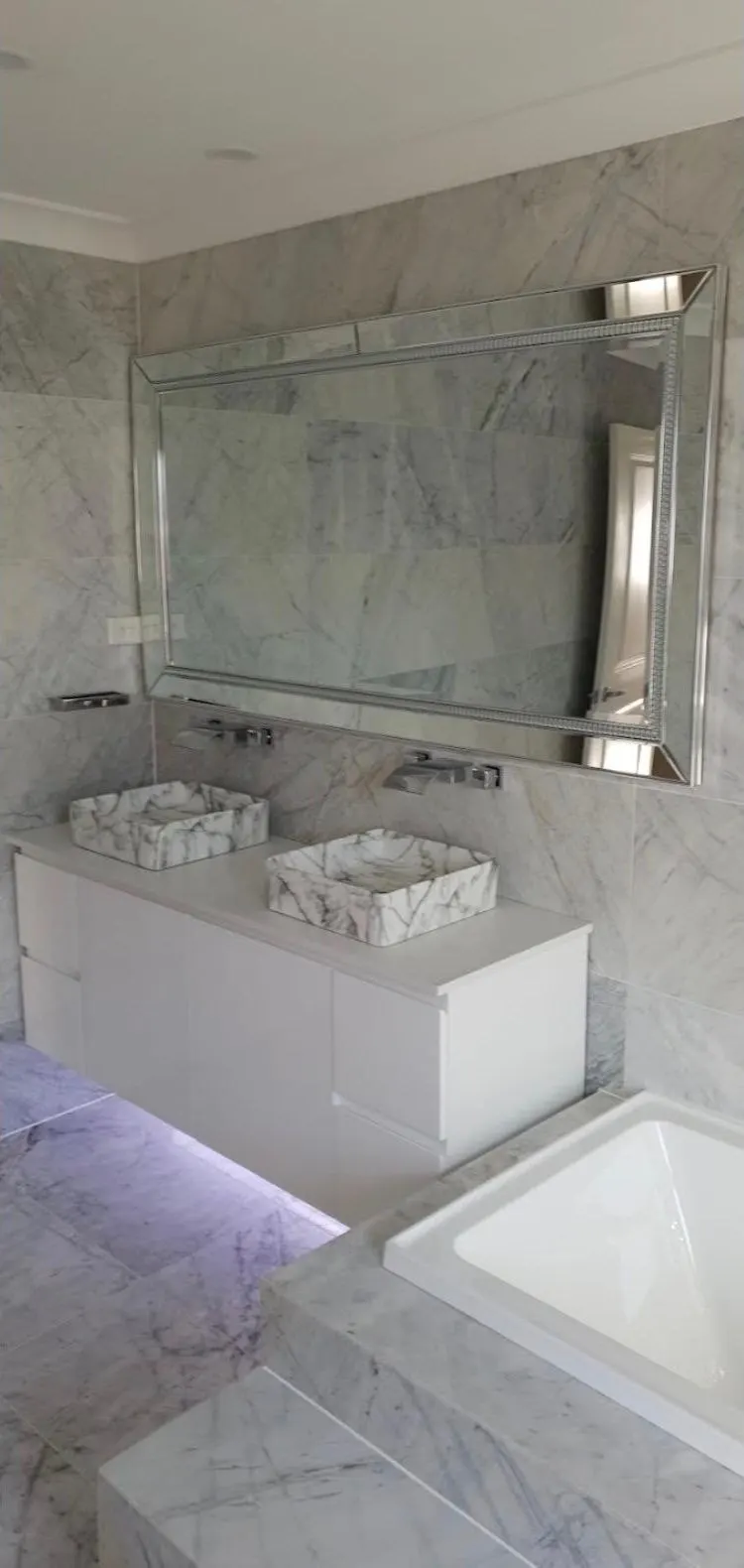 Marble bathroom with double basins on a floating vanity, built in bath and a bevelled mirror