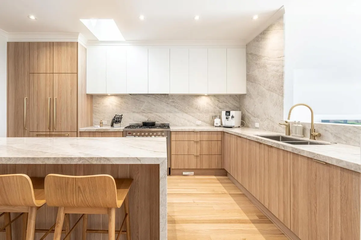 Timber and white kitchen with a stone island benchtop, brushed brass tapware and a skylight