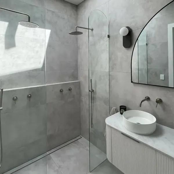 Walk in shower with a linear floor drain, arched frameless screen, fluted vanity and black arched mirror