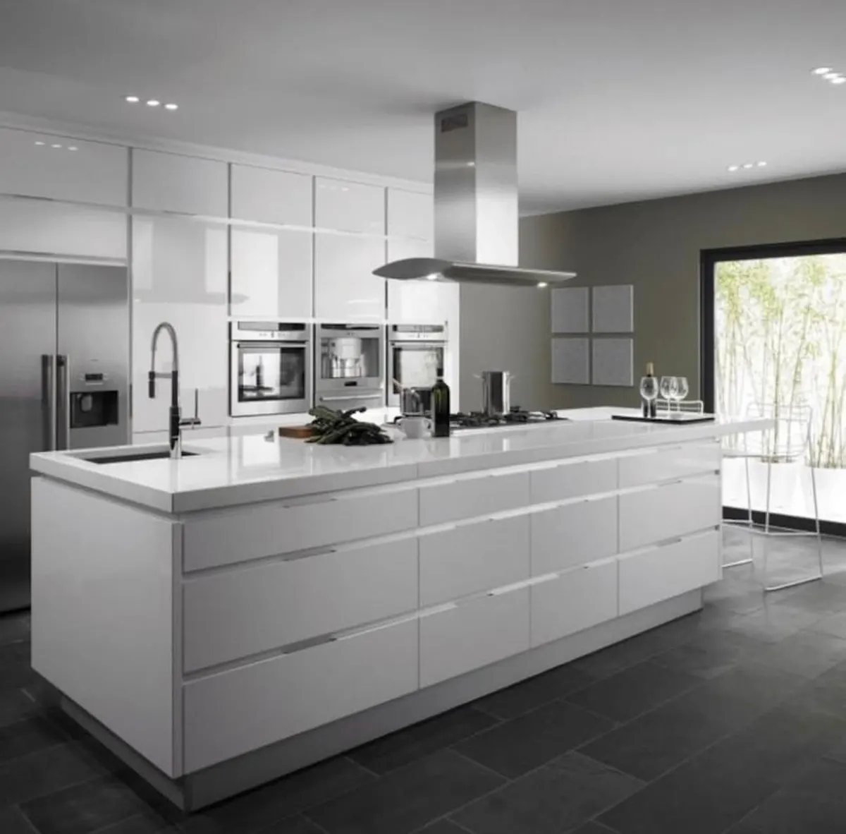 White gloss kitchen renovation with a large island, island cooktop with stainless steel rangehood and integrated ovens