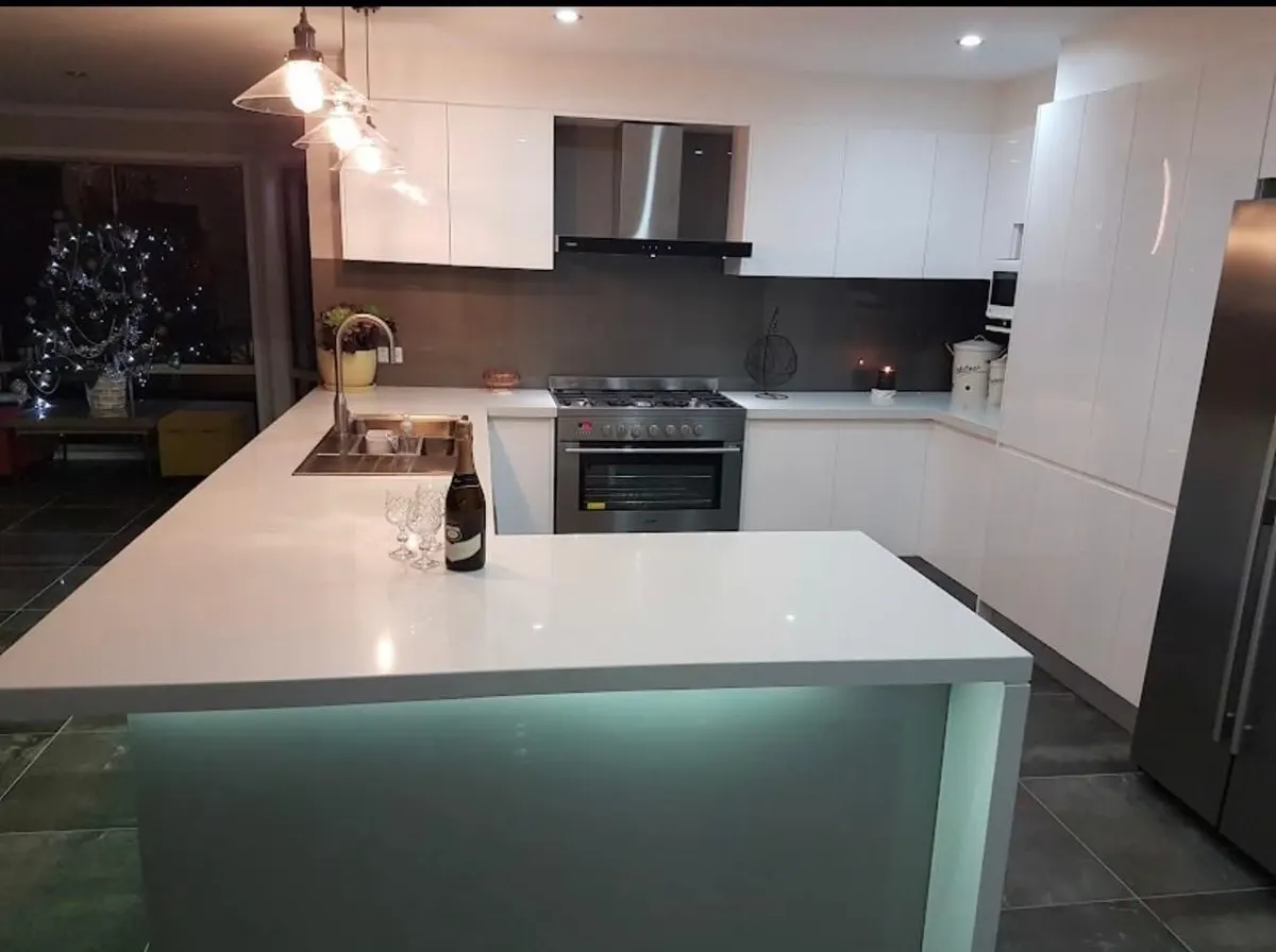 White kitchen renovation with a stone waterfall island lit from underneath, pendant lights and dark floor tiles