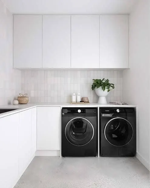 Modern white laundry with side by side washer and dryer under the benchtop, handleless overhead cabinets and tiled splashback