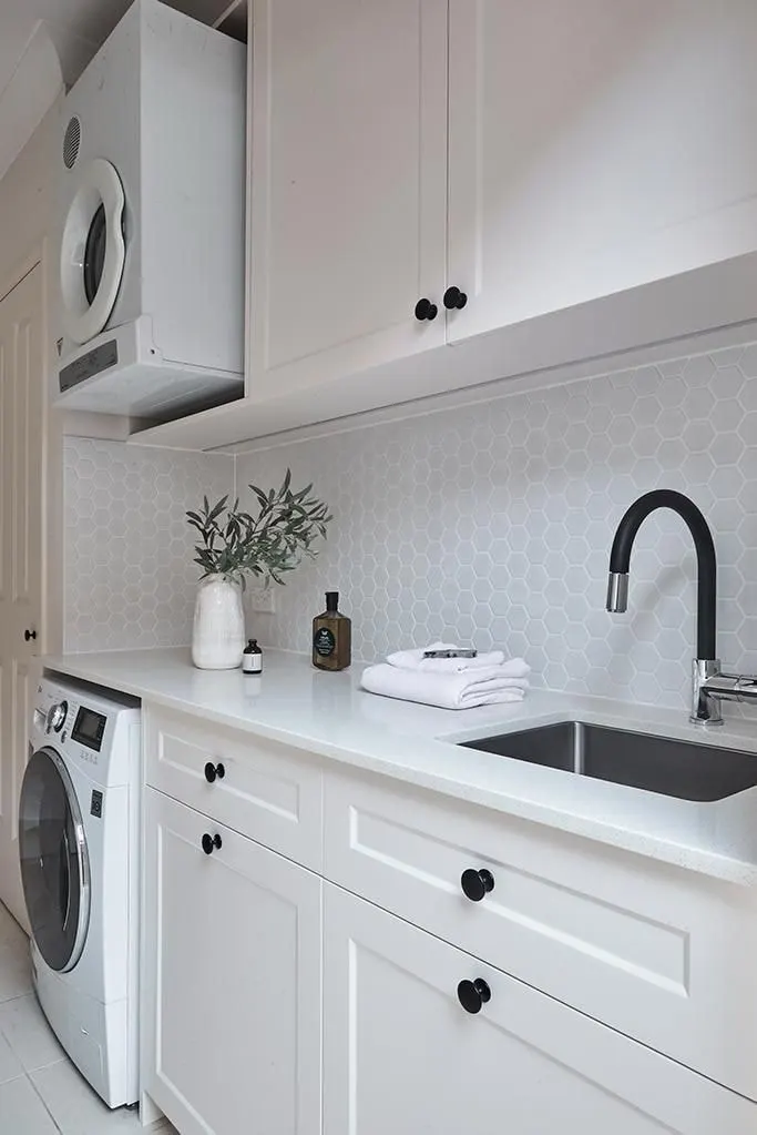 White shaker style laundry with a stacked dryer, hexagon tile splashback, undermount sink and black tapware